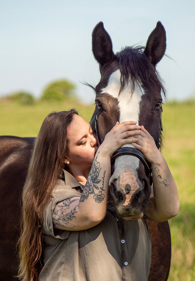 Eine Frau küsst ein Pferd, während sie liebevoll dessen Kopf hält.