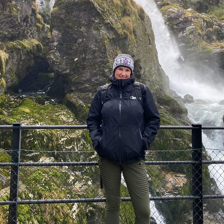 Person steht an einem Wasserfall, umgeben von Felsen und üppigem Grün.